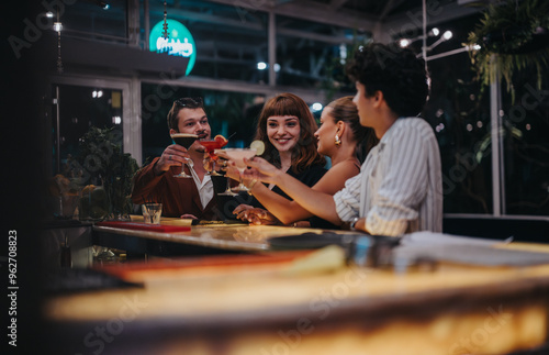 Group of friends socializing and raising cocktails at a stylish bar. They are smiling and enjoying a lively evening filled with laughter and good company.