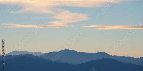 Silhouettes of mountains against a pale blue sky with clouds