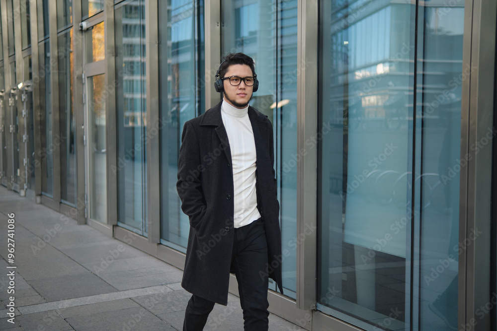 Fototapeta premium Young man walking in a city with headphones on