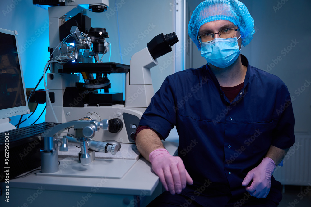 Embryologist in protective gear sits near advanced lab equipment Embryologist in protective gear sits near advanced lab equipment