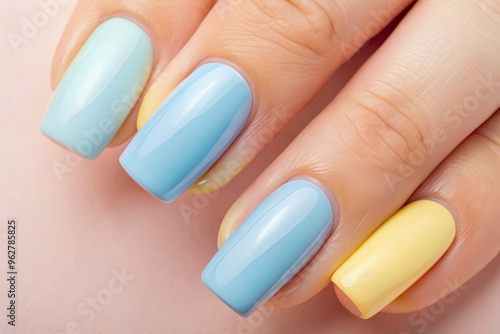 Pastel Blue And Yellow Painted Fingernails With Glossy Finish, Set Against A Pale Pink Background photo