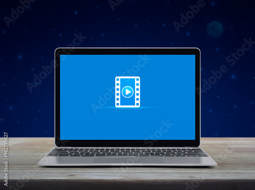 Play button with movie flat icon on modern laptop computer monitor screen on wooden table over fantasy night sky and moon, Business cinema online concept