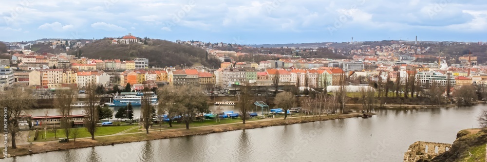 Obraz premium Panoramic view of Prague's colorful riverfront buildings and hills during early spring, highlighting urban tourism and scenic travel