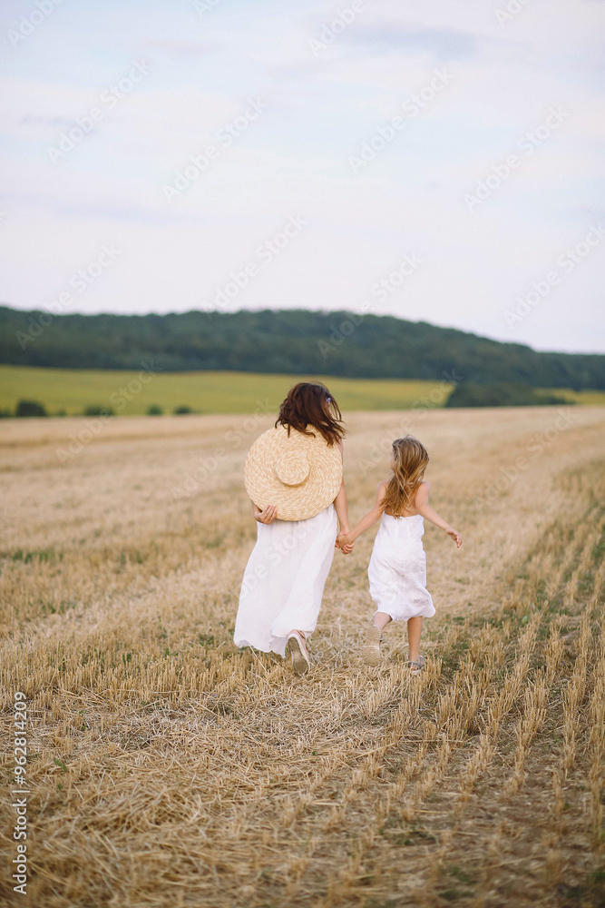 Happy mother and daughter in summer dresses running on the field Happy mother and daughter in summer dresses running on the field