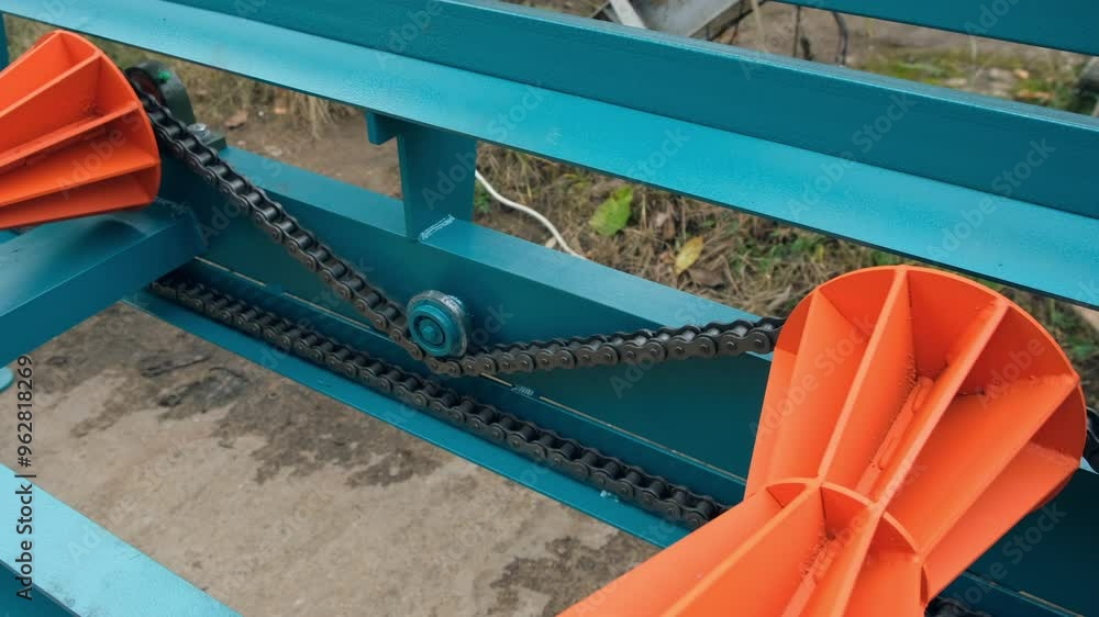 Chain conveyor belt moving along plastic orange rollers to move wooden logs. Automated mechanism of industrial equipment in modern plant. Woodworking, metalworking industry production manufacturing.