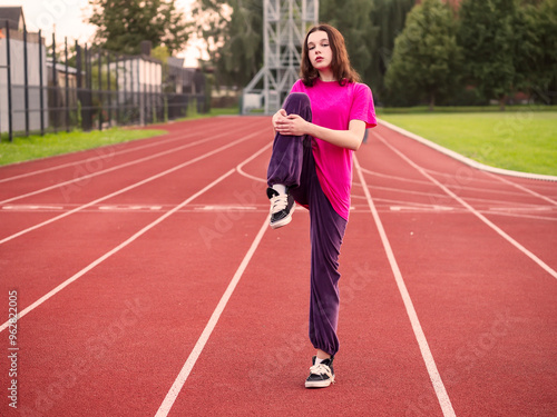 Young teenager girl doing stretches on a running track before run work out. Sport and healthy life style. Selective focus. Athletic routine in a public park fitness area.