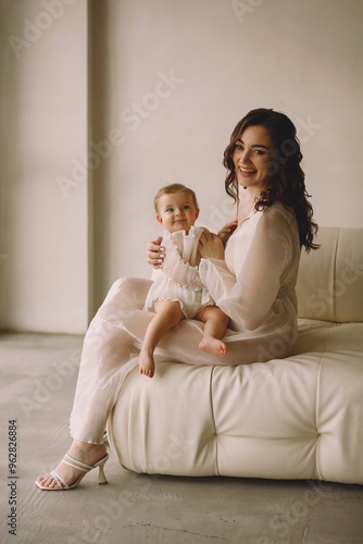 Mother playing with newborn baby girl while posing in the studio. Happy infant and mom. Family look