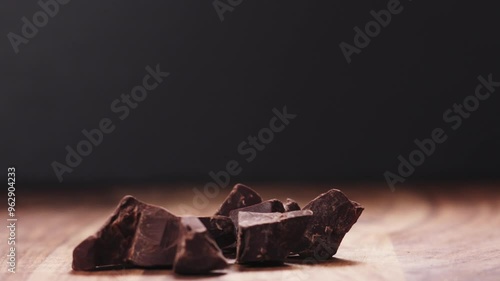 Slow motion closeup dark chocolate chunks falling on wood table