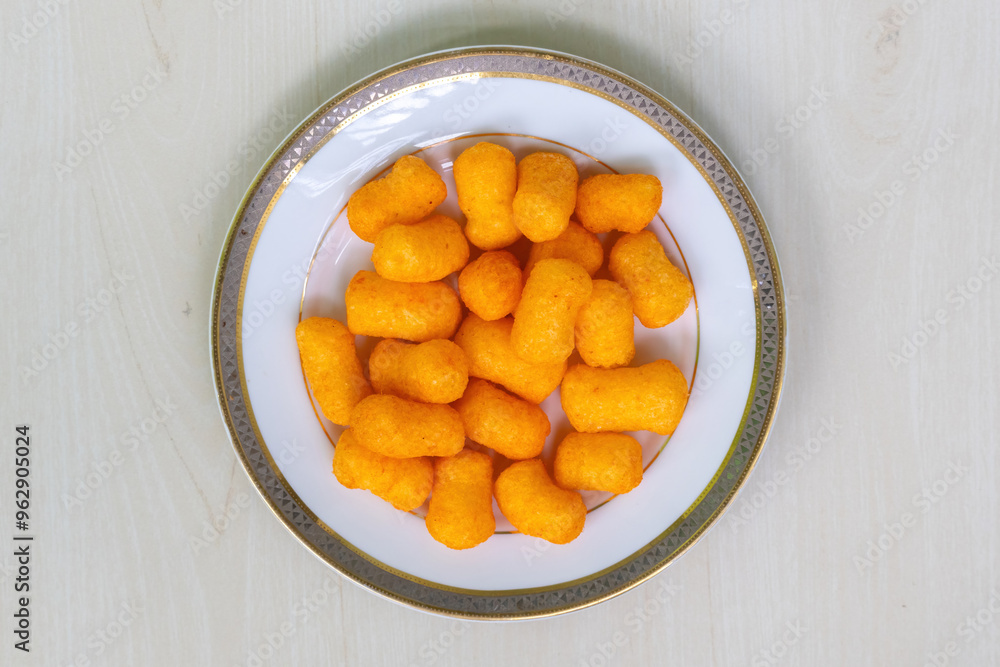 Crispy cheese flavored snacks crackers chips on a white plate on light a wooden surface. Top view. Crispy cheese flavored snacks crackers chips on a white plate on light a wooden surface. Top view.