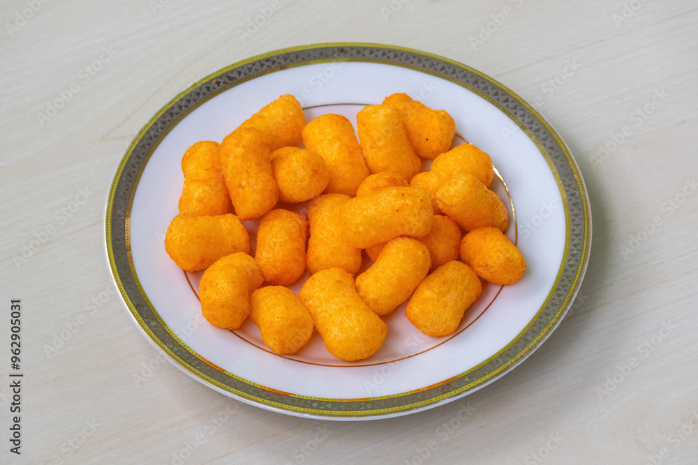 Cheese flavored snacks crackers chips on a white plate on light a wooden background. Cheese flavored snacks crackers chips on a white plate on light a wooden background.
