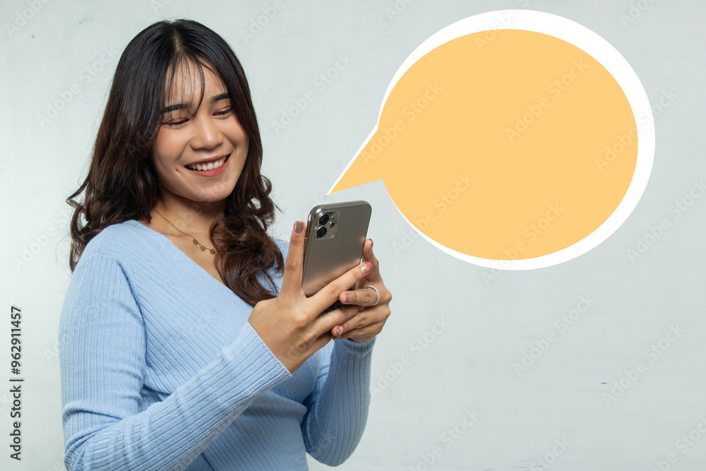 A girl standing replying to a message on her mobile phone with a smile, use of long hair woman advertising with talk box isolated on orange space A girl standing replying to a message on her mobile phone with a smile, use of long hair woman advertising with talk box isolated on orange space