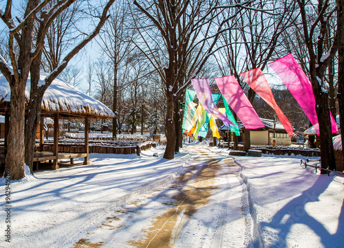 Yongin-si, Gyeonggi-do, South Korea - February 04, 2021: Colorful cloth are being hung on a line with snow covered thatched house and pavilion at Korean Folk Village photo