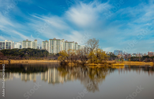 Suwon-si, Gyeonggi-do, South Korea - March 09, 2021: Spring view of willow trees on reservoir at Manseok Park with the background of highrise apartments