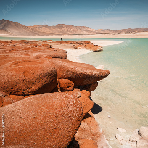 The striking red rock formation of Piedras Rojas stands out against the turquoise water, showcasing the unique landscape of the 4000-meter-high Andean altiplano near San Pedro de Atacama in Chile. photo