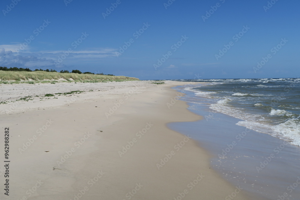Obraz premium An diesem sonnigen Sommertag branden Wellen an einem ruhigen Abschnitts des Strands Sandhammaren in Ystad in der schwedischen Provinz Schonen. Der Strand wird von einem Dünengürtel begrenzt.