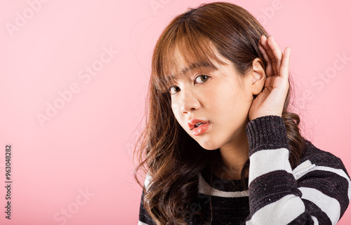 Asian portrait beautiful cute young woman teen smiling overhearing listening sound to gossip with attention with her hand on ear studio shot isolated on pink background with copy space hearing gesture