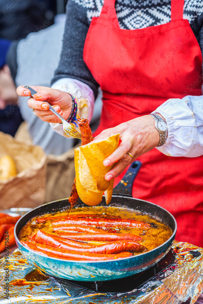 Fototapeta premium A Basque farmer (Baserritarra) frying Txistorra (fresh chorizo) to prepare Bocadillo de Txistorra, a traditional street food served during the Day of Saint Thomas.