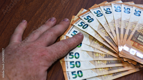 фотографія Male's Hand Holding EURO Banknotes on Brown Wooden Table