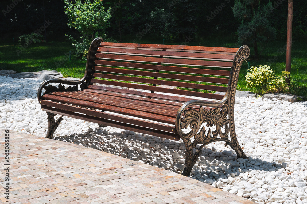 A beautiful wooden decorative bench in a city park against the backdrop of trees.