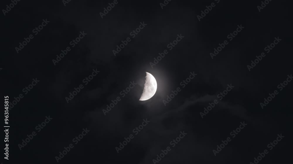 Moon in first quarter phase surrounded by misty dark clouds Moon in first quarter phase surrounded by misty dark clouds