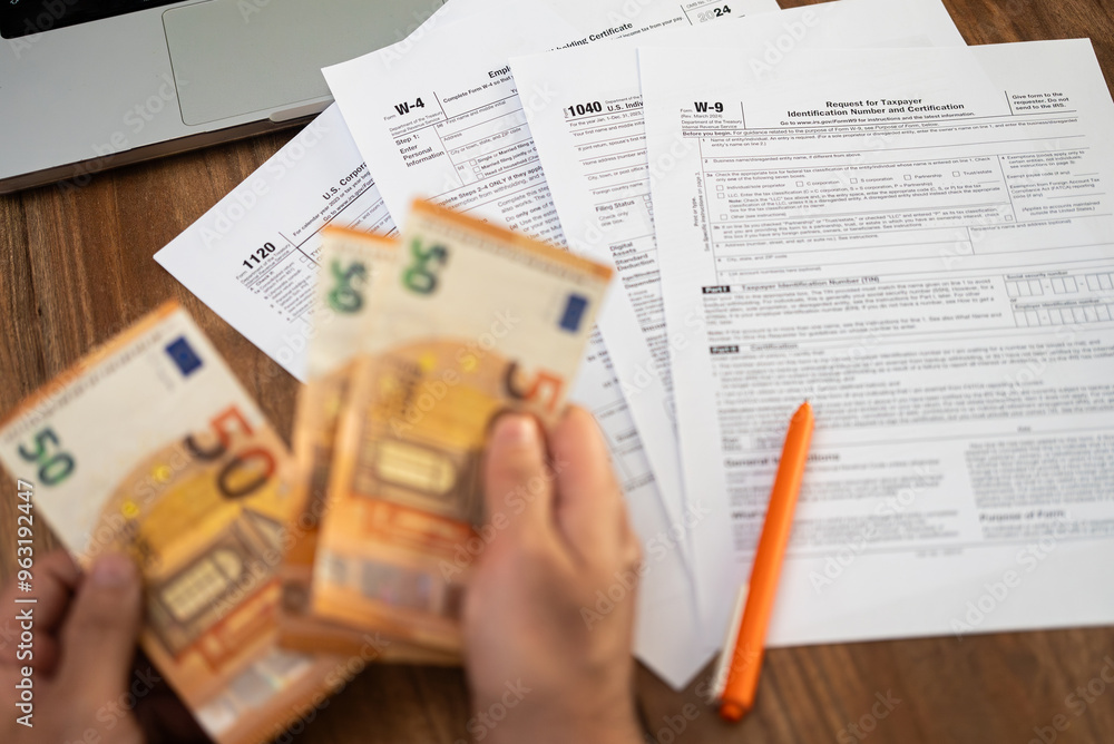Fototapeta premium Man freelancer counts euro banknotes preparing for filling various tax forms to report annual income avoiding penalties from government at workplace with laptop