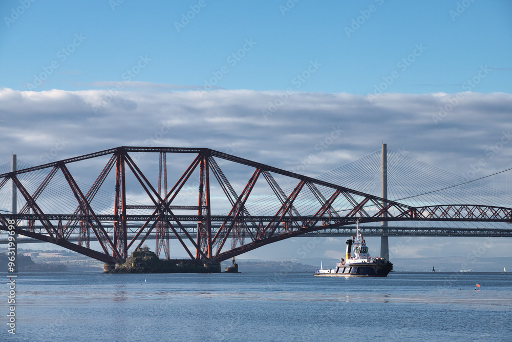 Obraz premium Tugboat Passing Under Forth Bridge with Parallel Cloud Formation in Scotland