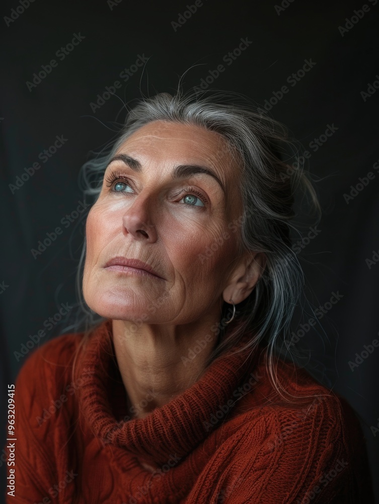 Fototapeta premium A woman with gray hair is wearing a red sweater and looking up. She has a serious expression on her face