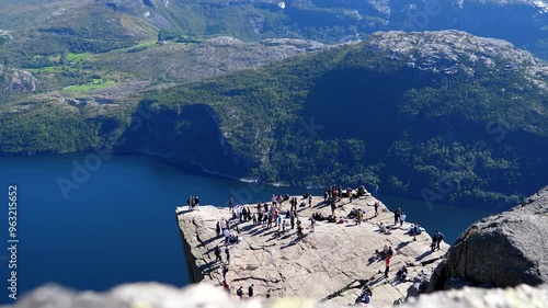 High angle view of people, hikers, tourists queueing for photos on corner spot on top of famous table like Pulpit Rock or Preikestolen in Norway on a beautiful sunny day.