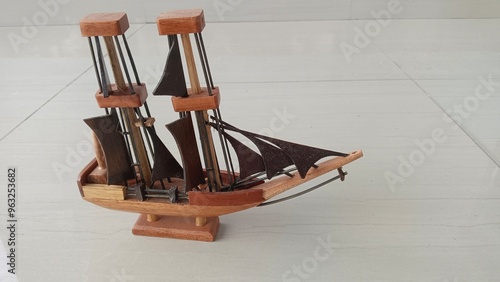 A wooden model ship with two masts, sails, and a wooden base. The ship is on a light-colored tiled floor. photo