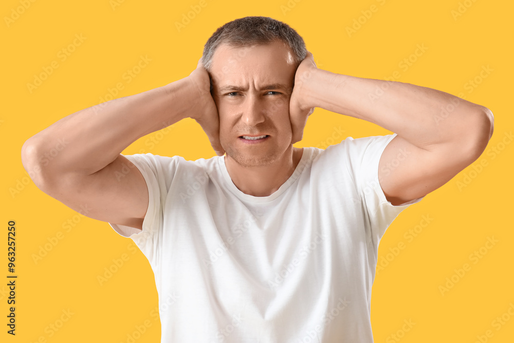 Portrait of stressed mature man suffering from loud noise on orange background Portrait of stressed mature man suffering from loud noise on orange background