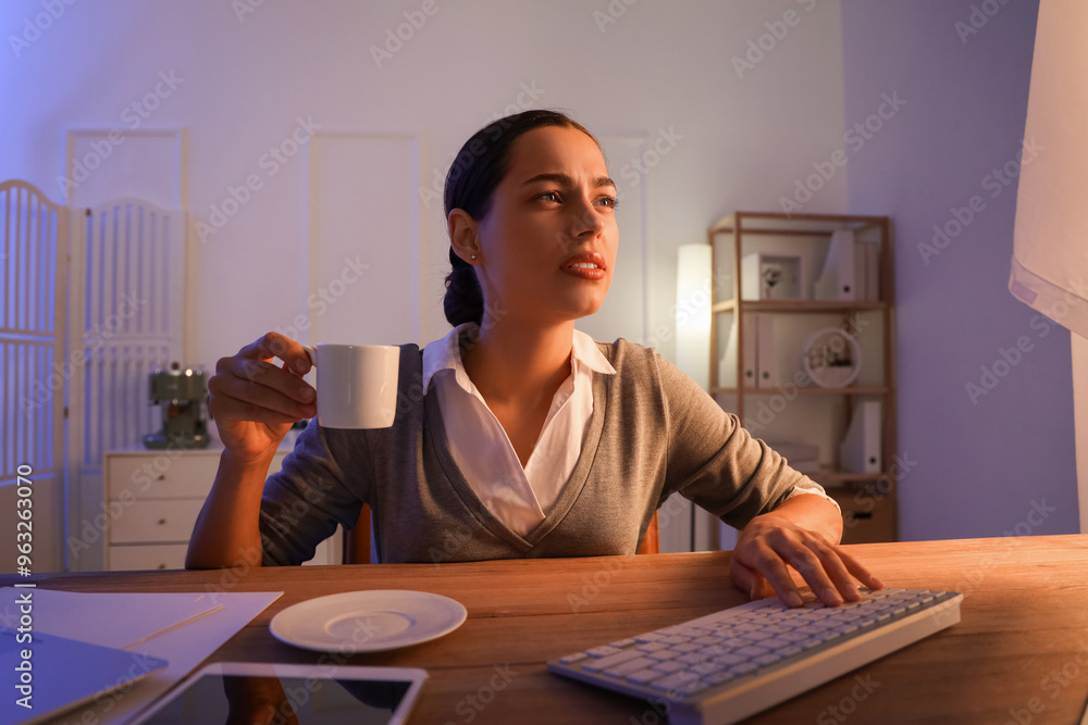 Tired young female programmer with cup of coffee working in office at night Tired young female programmer with cup of coffee working in office at night