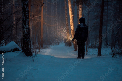 a man with a flashlight in his hand walks among the trees, illuminating his way at night