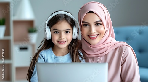 A Muslim mother and daughter smile as they use a laptop, creating a moment of connection.