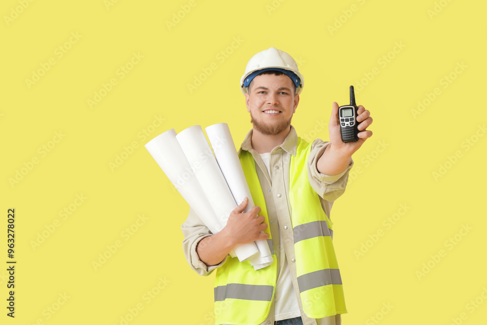 Male contractor with house plans and radio transmitter on yellow background Male contractor with house plans and radio transmitter on yellow background