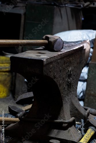 Close-up view of a vintage hammer resting on an anvil, set against a dimly lit workshop background, highlighting the textures and age of the metal tools.