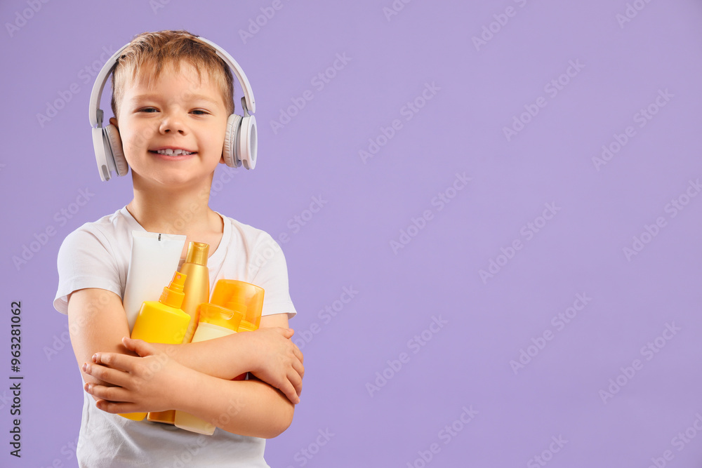 Cute little boy in headphones with bottles of sunscreen cream on lilac background Cute little boy in headphones with bottles of sunscreen cream on lilac background