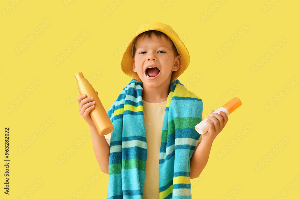 Cute little boy with bottles of sunscreen cream on yellow background Cute little boy with bottles of sunscreen cream on yellow background