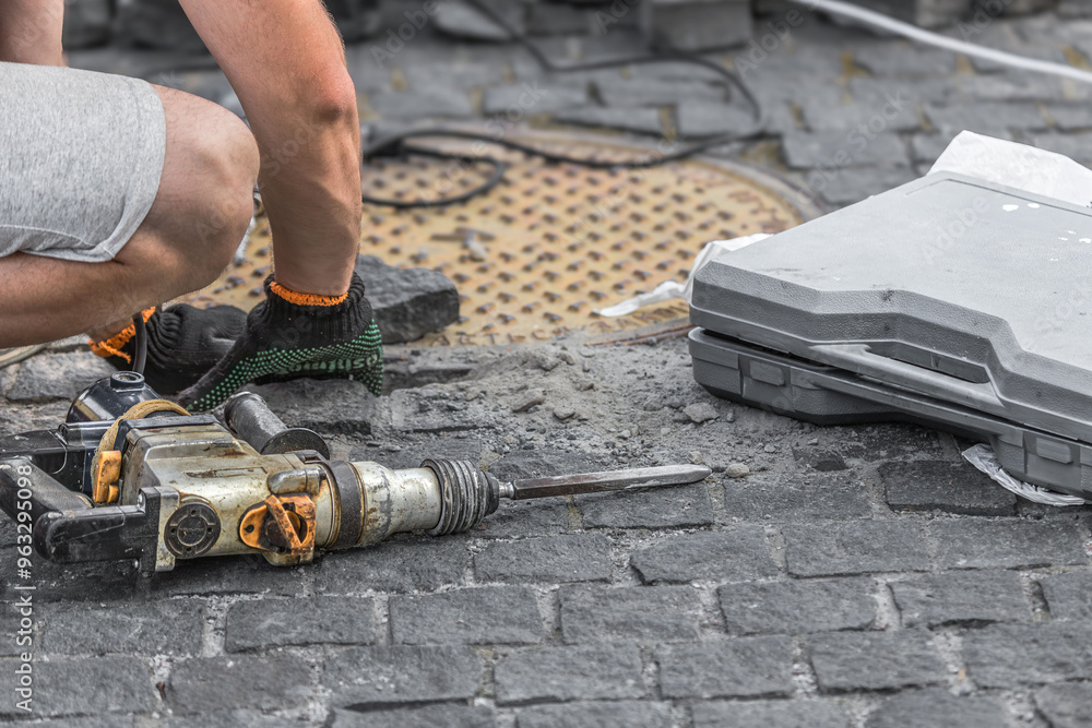 Industrial tool for repairing paving stones on the sidewalk. A man removes old cobblestones with a perforator. Drill, shovel, pickaxe and hammer on construction site. Road repair. Home tool. Industrial tool for repairing paving stones on the sidewalk. A man removes old cobblestones with a perforator. Drill, shovel, pickaxe and hammer on construction site. Road repair. Home tool.