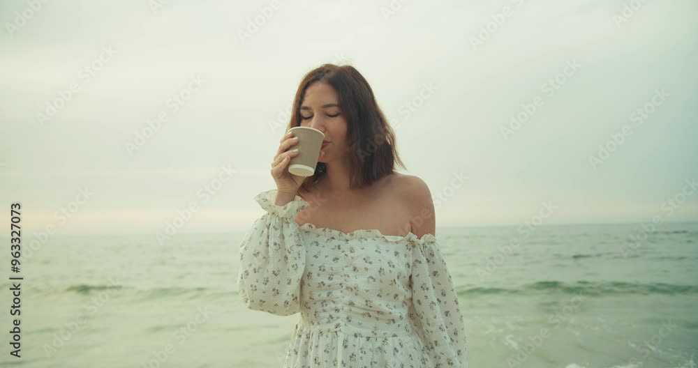 Happy brunette girl enjoying and drinking coffee from a paper cup in the morning on the beach in summer Happy brunette girl enjoying and drinking coffee from a paper cup in the morning on the beach in summer