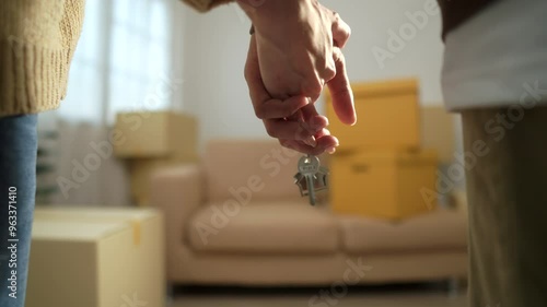 Close up shot hands of couple homeowner holding the house key and walking through inside the room with boxes and furniture background after moving to new house, relocating apartment concept.
