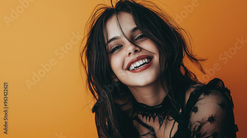 A bright portrait of a young woman wearing a vampire attire and smiling cheerfully against a vibrant orange background.