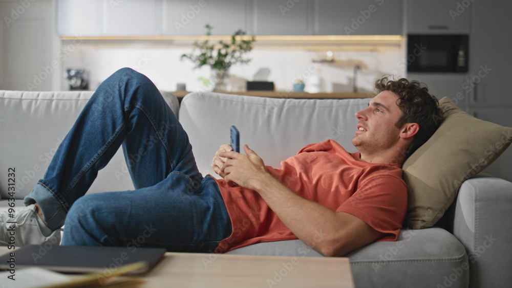 Lazy man browsing cellphone laying couch. Smiling guy putting down mobile phone Lazy man browsing cellphone laying couch. Smiling guy putting down mobile phone