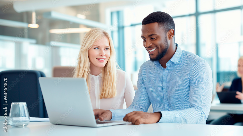 A cheerful team of multiethnic office workers gathered around a table in a conference room. An African man is explaining something on his laptop while a blonde woman attentively li A cheerful team of multiethnic office workers gathered around a table in a conference room. An African man is explaining something on his laptop while a blonde woman attentively li