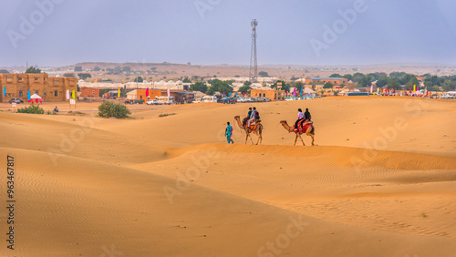 Tourist on camel safari at the Thar desert Jaisalmer, Rajasthan at sunset with view of camel caravan.