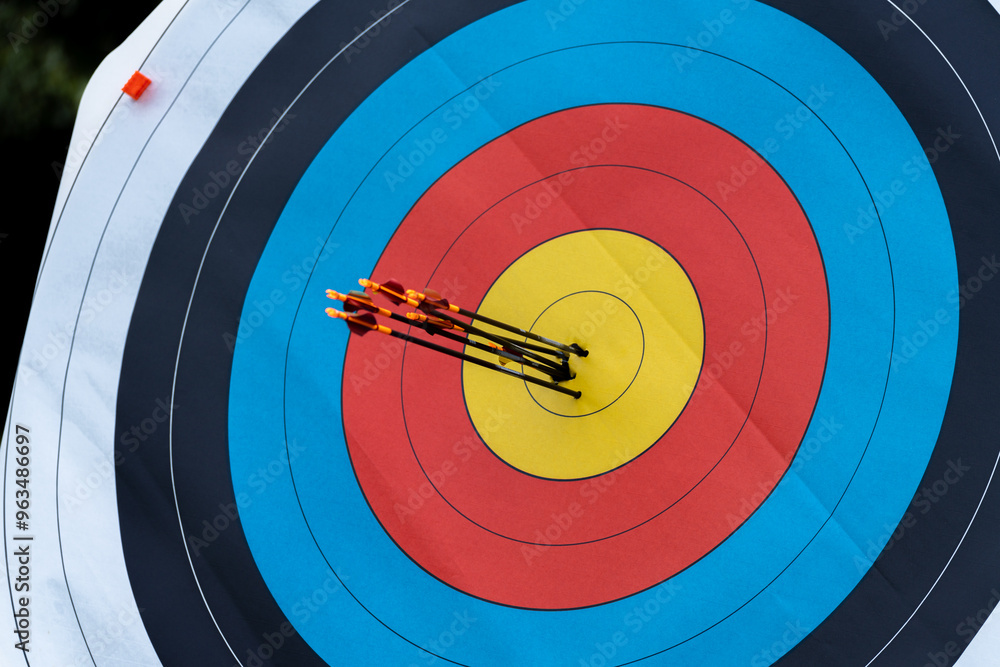 Near shot of archery target with six arrows in yellow gold hitting bulls eye successfully scoring Near shot of archery target with six arrows in yellow gold hitting bulls eye successfully scoring