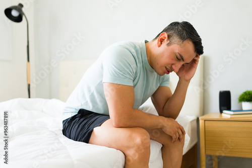 Unwell young man experiencing a severe headache while sitting on his bed at home