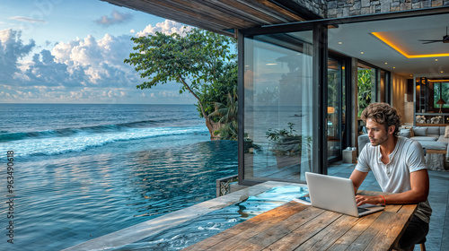 A man working on his laptop in a luxurious modern home with a stunning ocean view
 photo