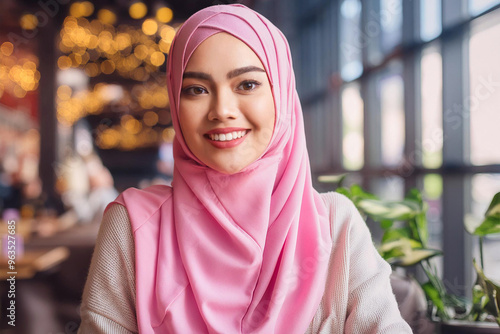 Portrait of a happy smiling young Arab Muslim woman wearing pink hijab in a cafe