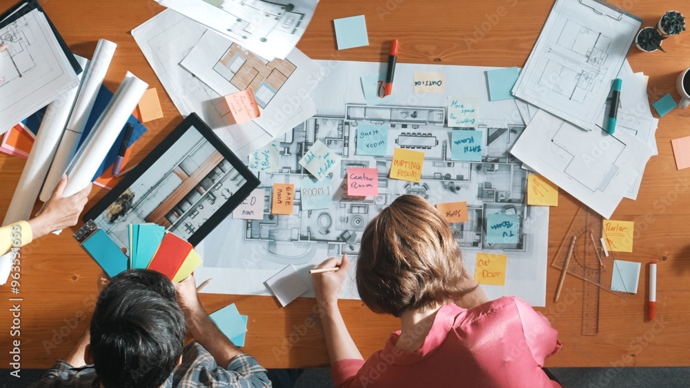Top view of engineer working together to design building construction while standing at meeting table with blueprint and notes. Top view of interior designer choosing color from palettes. Symposium. Top view of engineer working together to design building construction while standing at meeting table with blueprint and notes. Top view of interior designer choosing color from palettes. Symposium.
