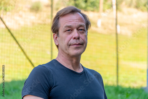 Portrait of a man 50-55 years old on a sunny day among green grass and trees.